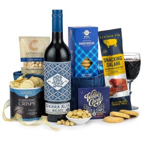 A deep blue woven tray filled with an array of savoury treats and a 75cl bottle of Sierra Alta Malbec